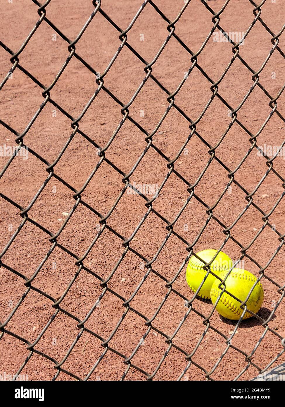 Pair of yellow softballs in dirt behind chain link fence Stock Photo