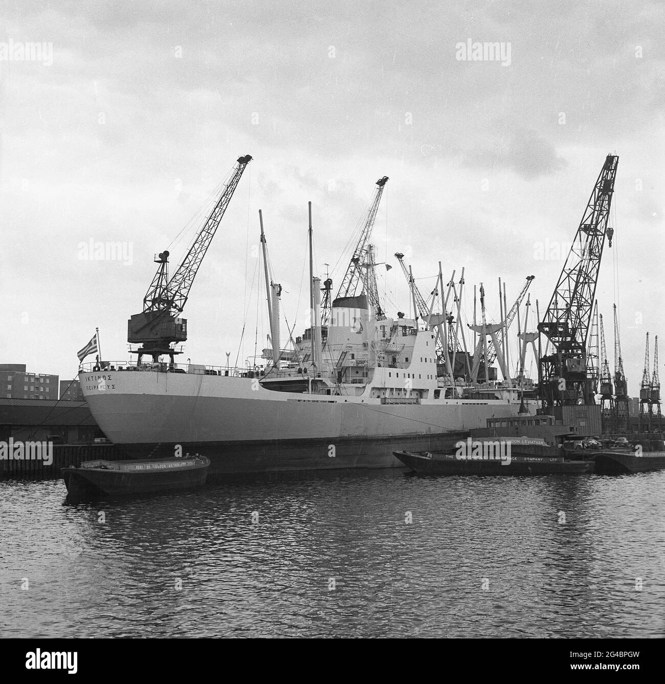 1960s, historical, Greek cargo ship, 'IKTINOS' moored at Tilbury Docks on  tthe river Thames at Tilbury Essex, England, UK, a part of the wider Port of London. Beside it, the PLA floating crane, London Leviathan, a self-propelled crane barge, built in Amsterdam in 1965 for the Port of London Authority.  Also seen is a tug of the Mercantile Lighterage Co. The cargo ship IKTINOS was built in July 1969 by Doxford & Sunderland Shipbuilding & Engineering Co., Ltd., Sunderland, UK, for Lineas Interoceanicas S.A. under the Greek flag. Stock Photo