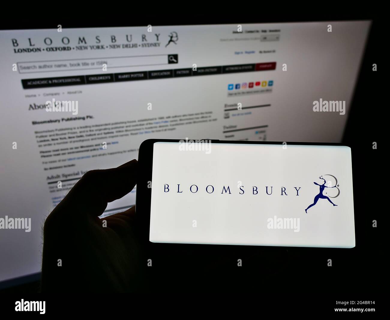 Person holding mobile phone with logo of British publisher Bloomsbury Publishing plc on screen in front of business web page. Focus on phone display. Stock Photo