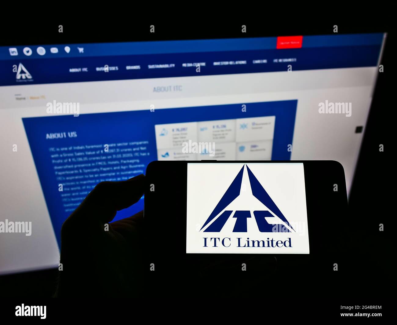 Person holding smartphone with logo of Indian conglomerate ITC Limited on screen in front of website. Focus on phone display. Stock Photo