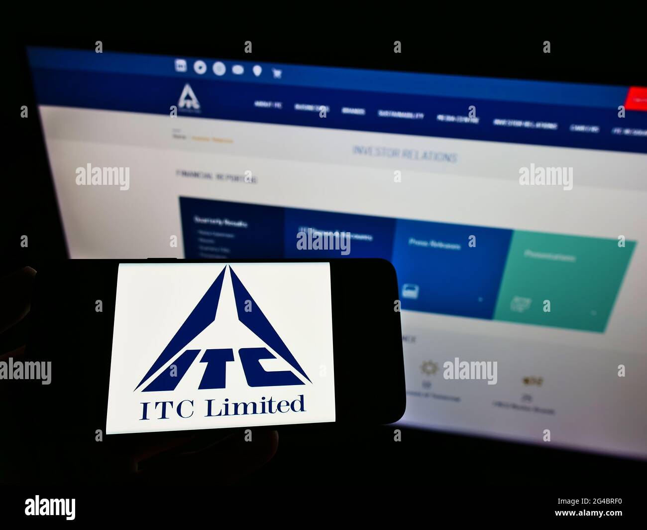 Person holding mobile phone with logo of Indian conglomerate ITC Limited on screen in front of business web page. Focus on phone display. Stock Photo