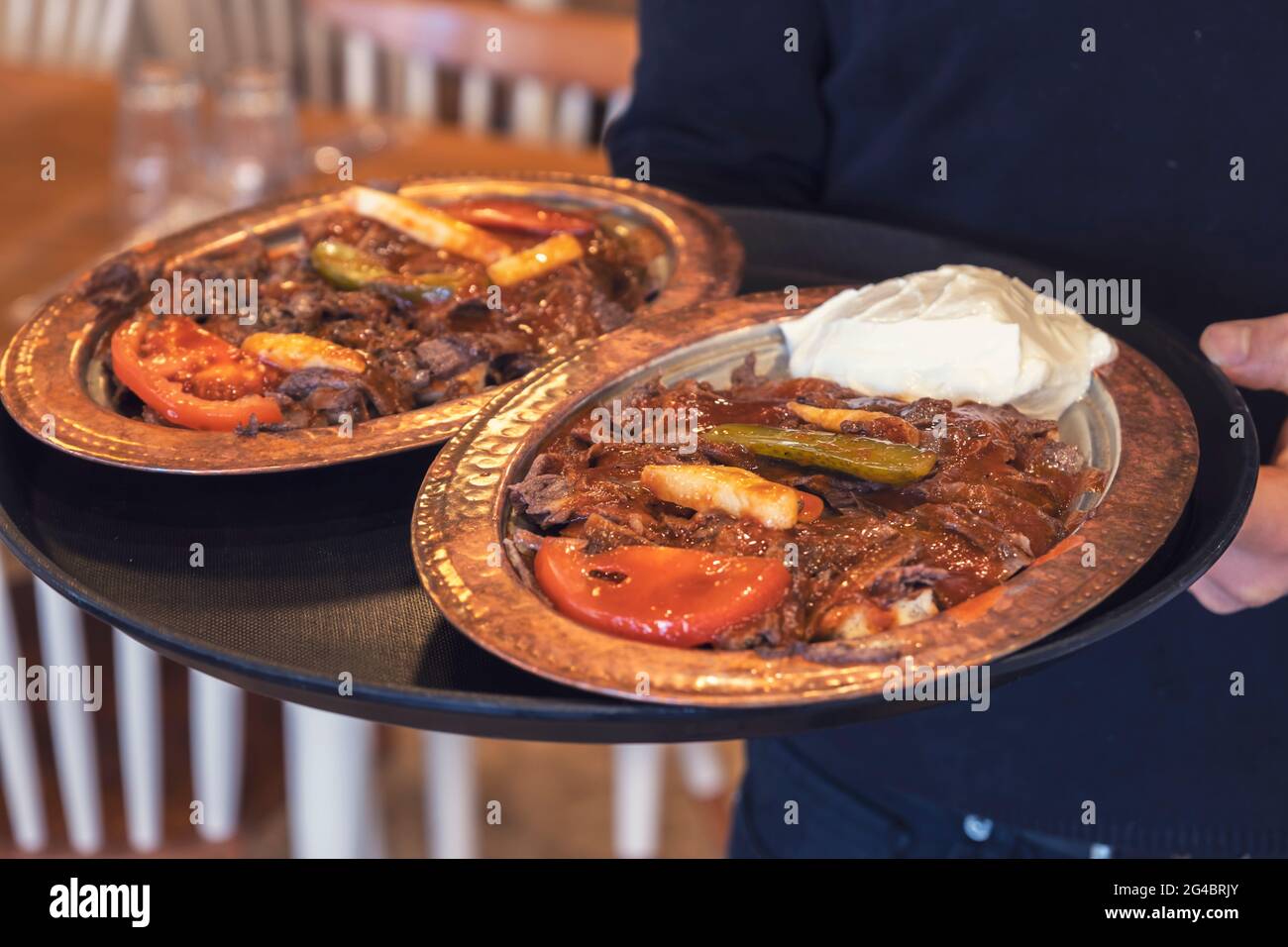 Waiter holding Iskender Kebab plates with food serving guests in a restaurant. Stock Photo