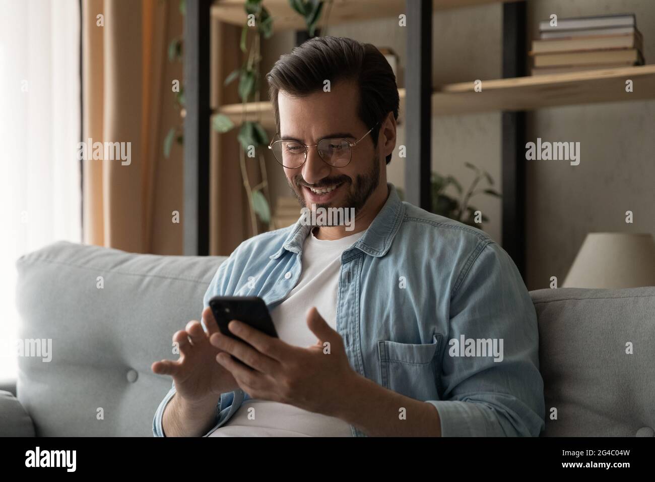 Happy young man in eyeglasses using smartphone. Stock Photo