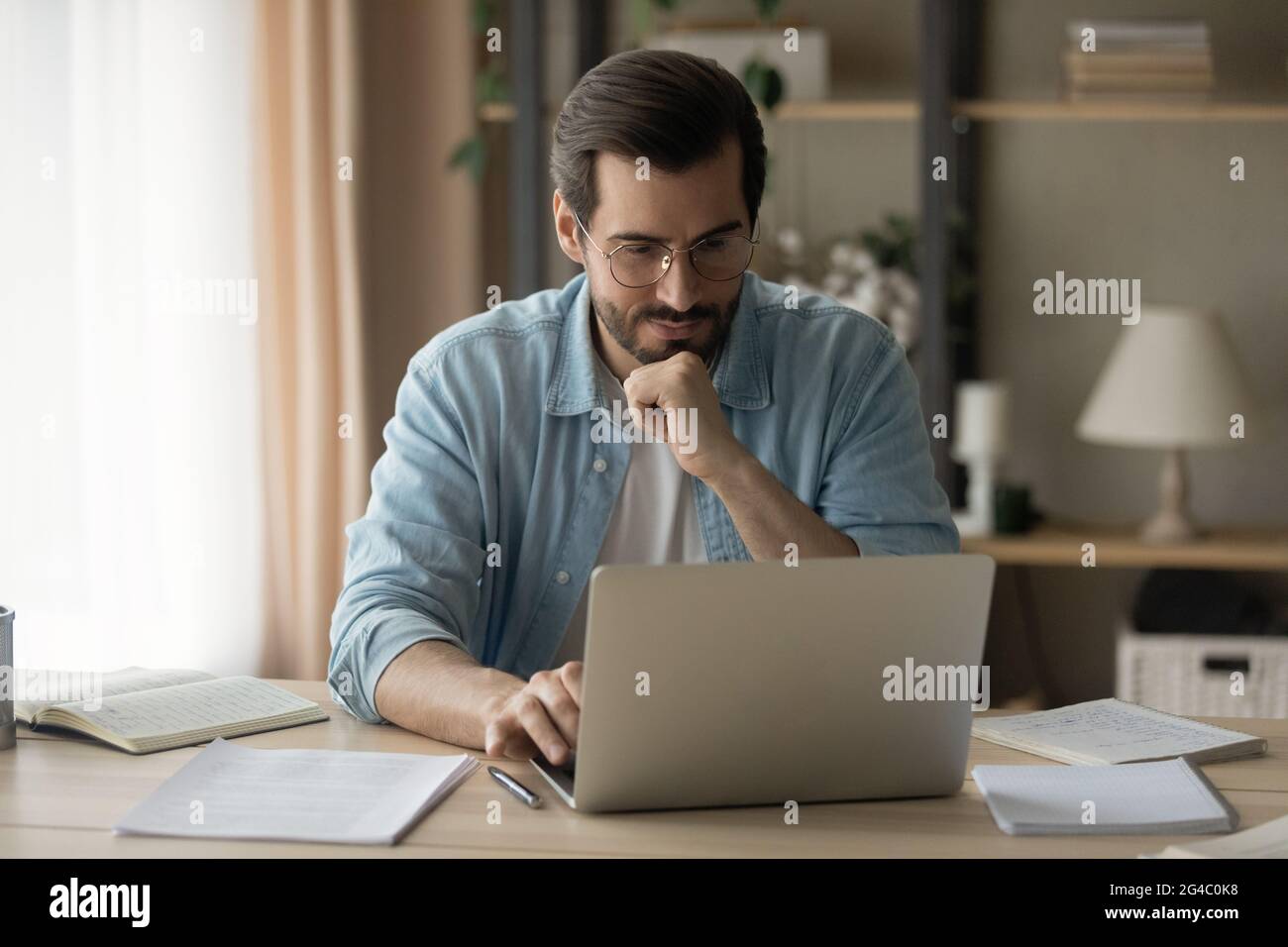 Concentrated happy young business man working on computer at home. Stock Photo