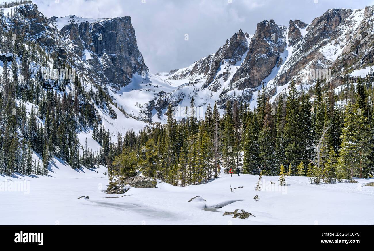 Spring Mountains - Lakes are still frozen in late May. A few brave visitors hiking along snow-covered Dream Lake towards high peaks in RMNP, CO, USA. Stock Photo