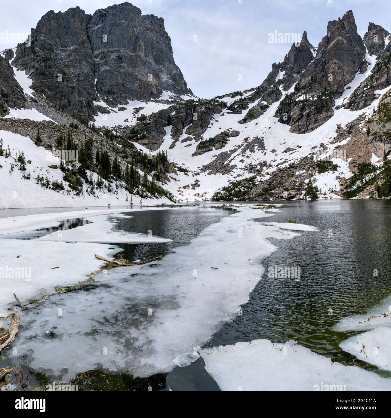 Emerald Lake - A wide-angle Spring view of half-frozen Emerald Lake at base of formidable Hallett Peak and rugged spires of Flattop Mountain. RMNP. Stock Photo