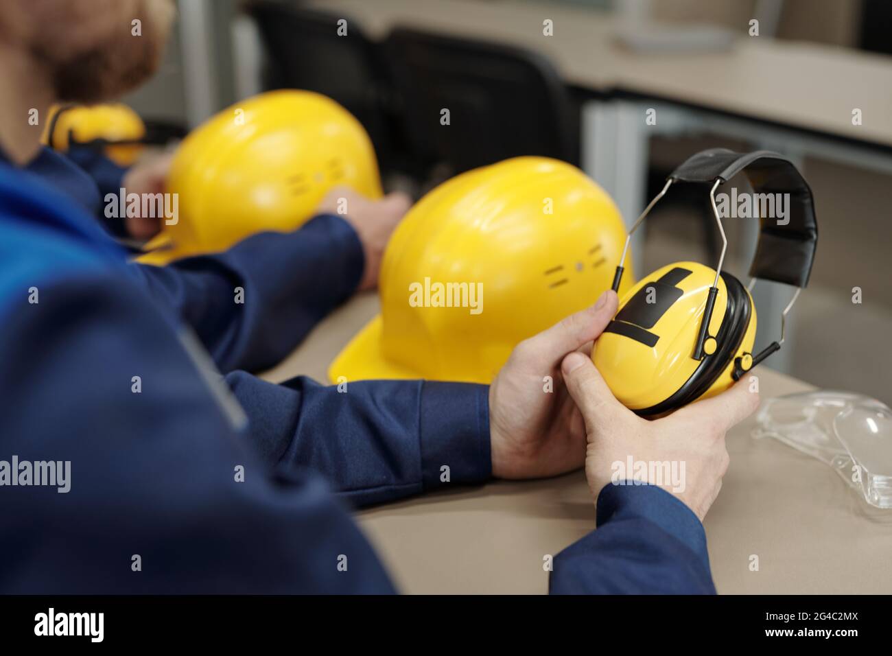 Close-up of unrecognizable factory worker sitting at table with hardhat and goggles and holding sound-proof protective headphones Stock Photo