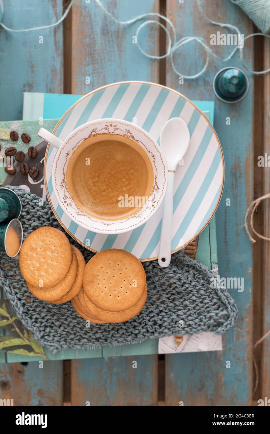 Cup of hot coffee on a ceramic turquoise striped dish with some piled cookies around over two bluish books. Stock Photo
