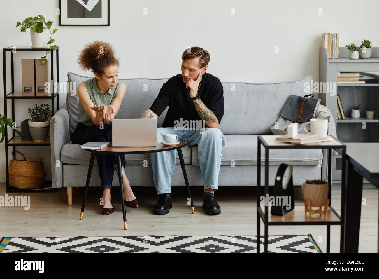 Two business people sitting on sofa using laptop and discussing online presentation at office Stock Photo