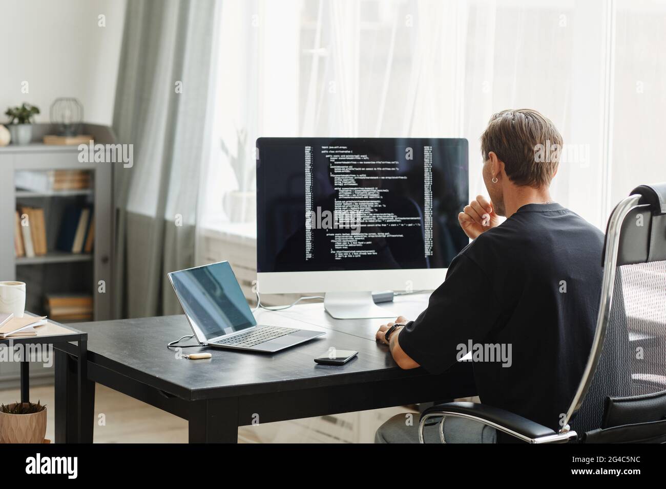 Rear view of computer programmer sitting at the table in front of computer  monitor and developing software at office Stock Photo - Alamy