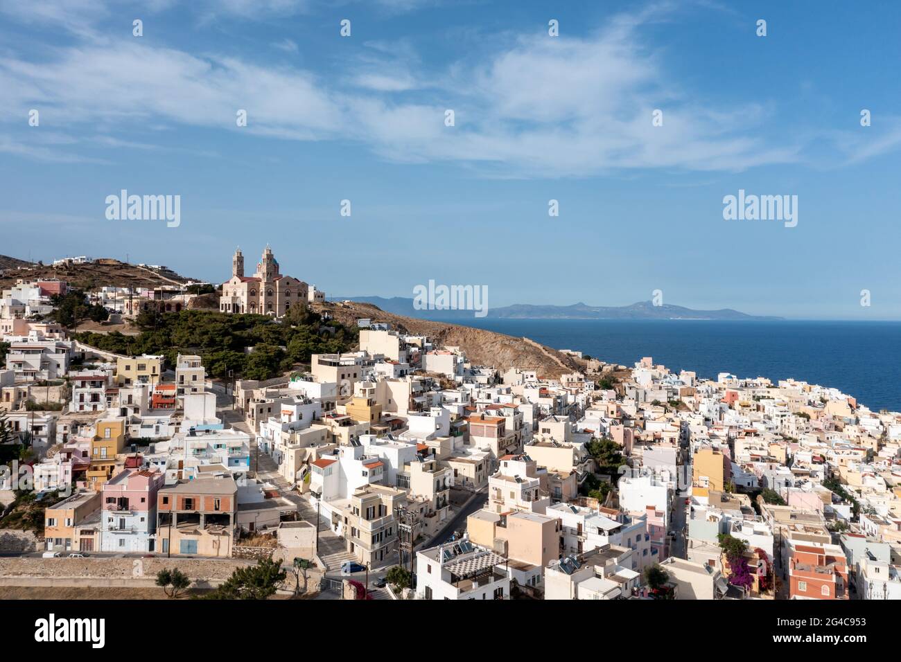 Ano Siros town cityscape, Syros island, Greece, aerial drone view. The Church of Resurrection uphill, calm sea and cloudy blue sky background. Stock Photo