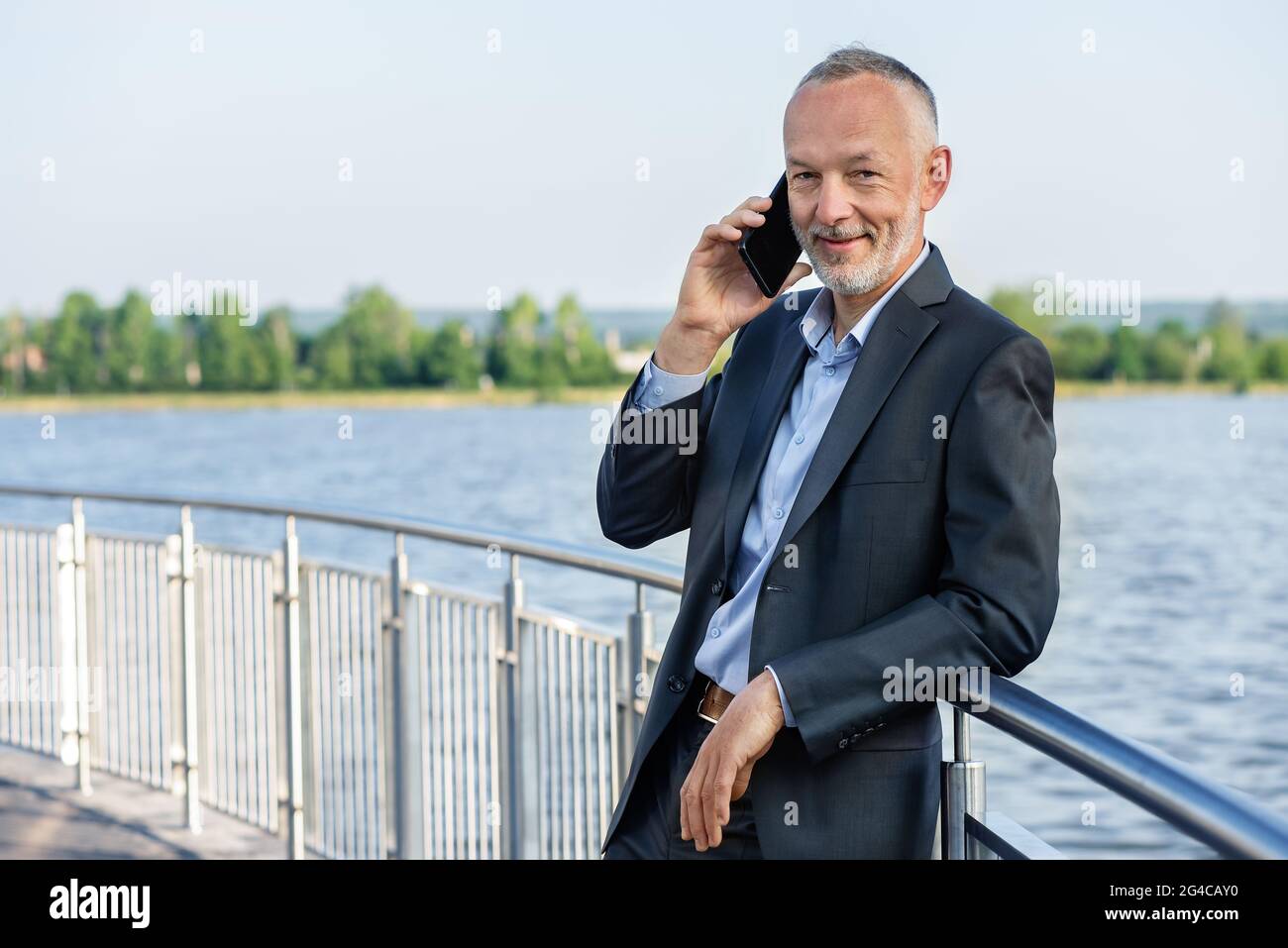 Smiling businessman in a gray suit with a smartphone. Stock Photo