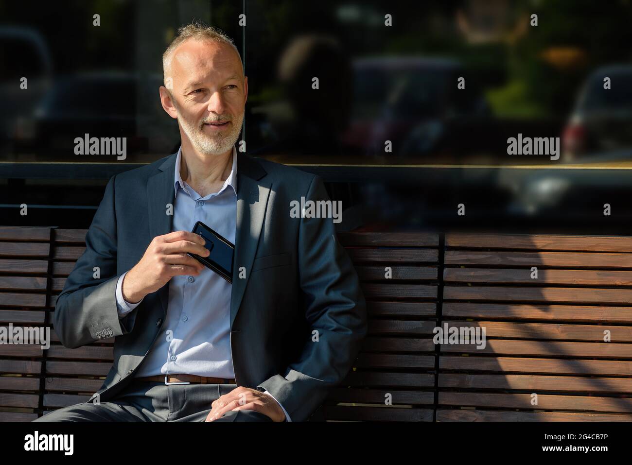The man in a gray suit with a smartphone sitting on a bench. Stock Photo