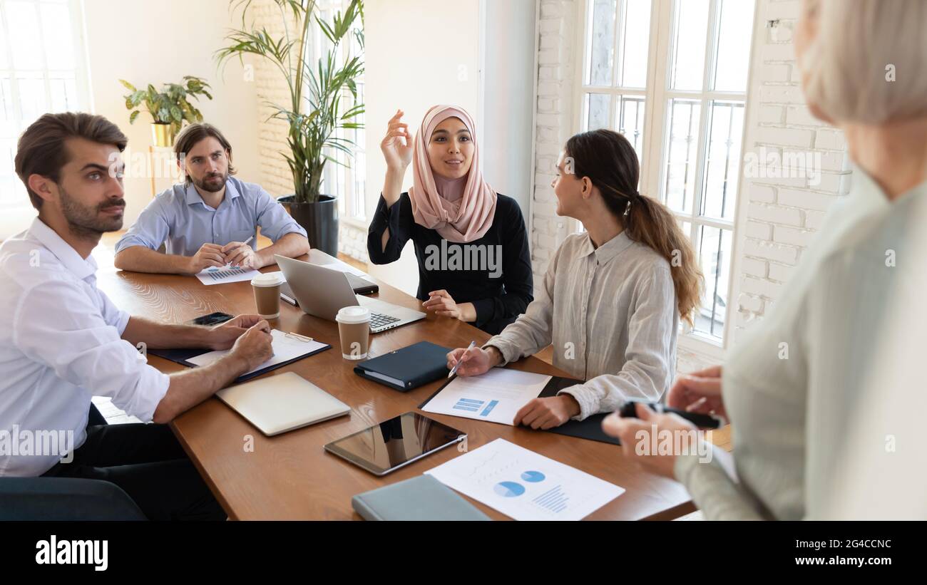 Asian muslim businesswoman with raised hand asking question to coach Stock Photo