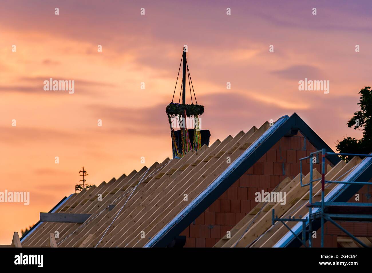 A roof truss of a new building with a topping-out wreath at sunset Stock Photo