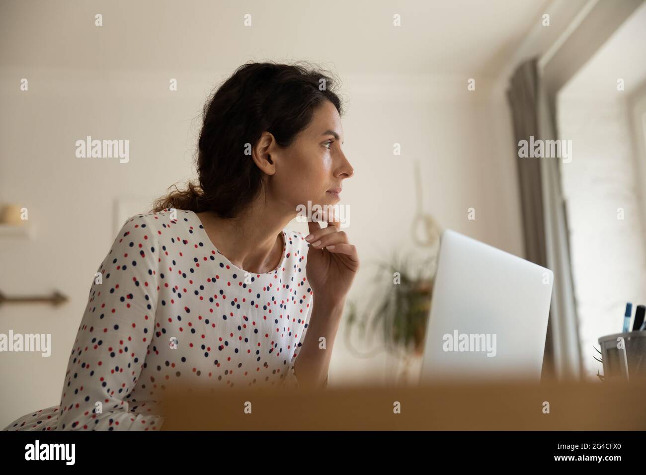 Thoughtful businesswoman touching chin, pondering business project, using laptop Stock Photo