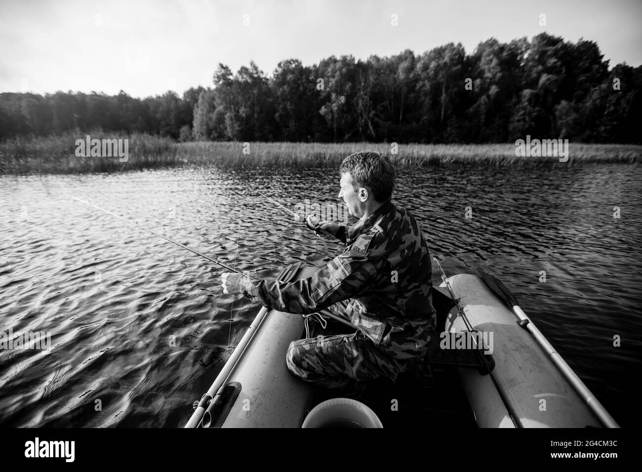 A Man in a Camouflage Suit and Cap Sits in a Boat with a Fishing
