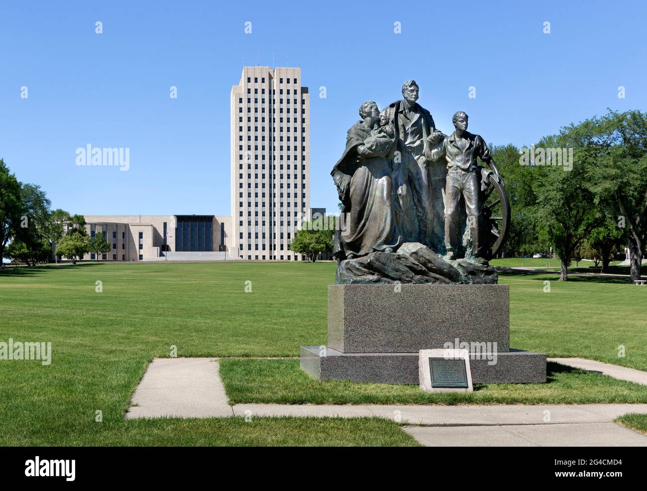 1946 bronze sculpture Pioneer Family Statue by Avard Fairbanks and the 1934 Art Deco North Dakota State Capitol building in Bismarck, North Dakota. Stock Photo