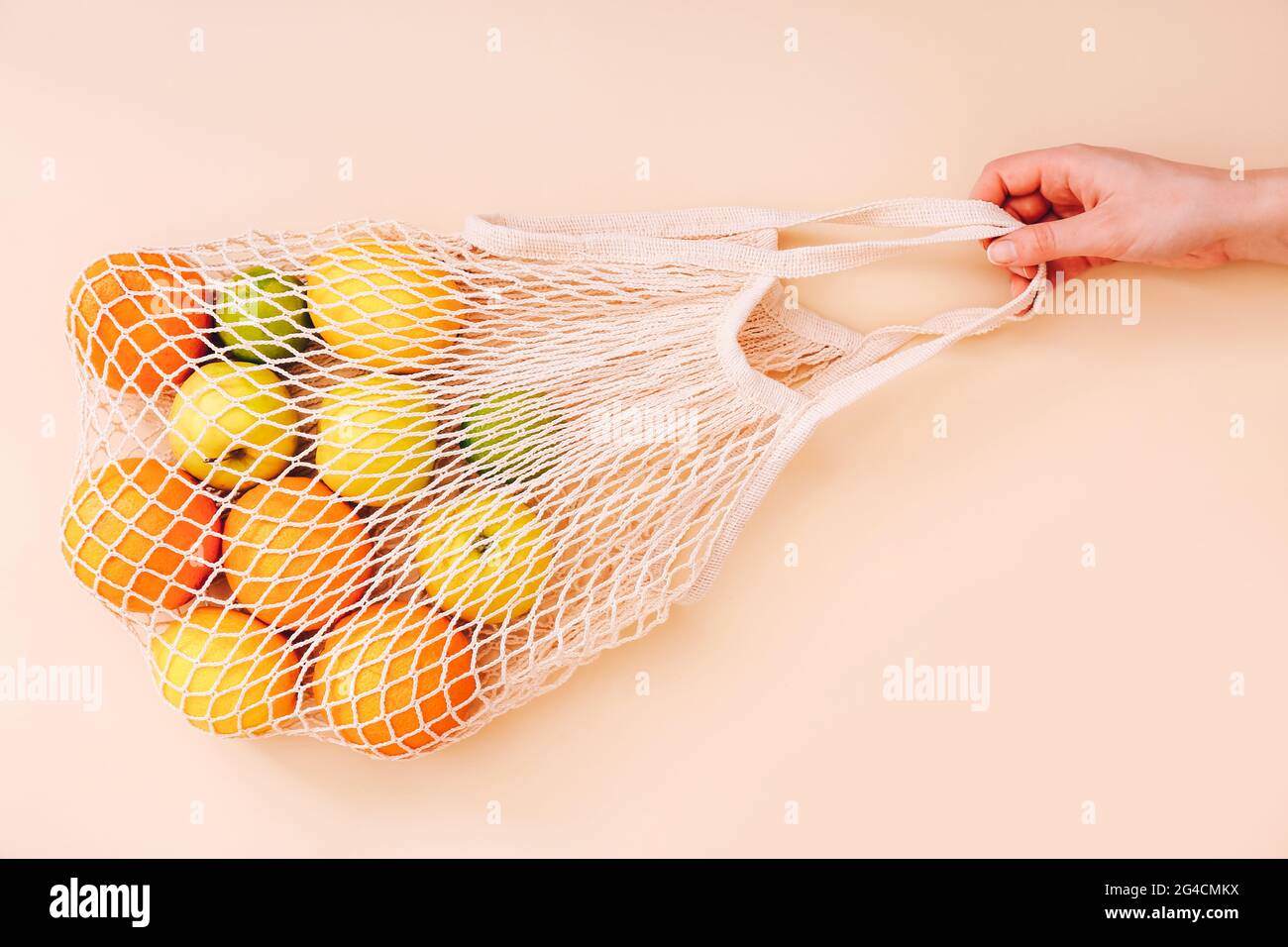 Female hand holding mesh eco bag with fruits on light background. Healthy clean eating. Eco shopping concept. Stock Photo