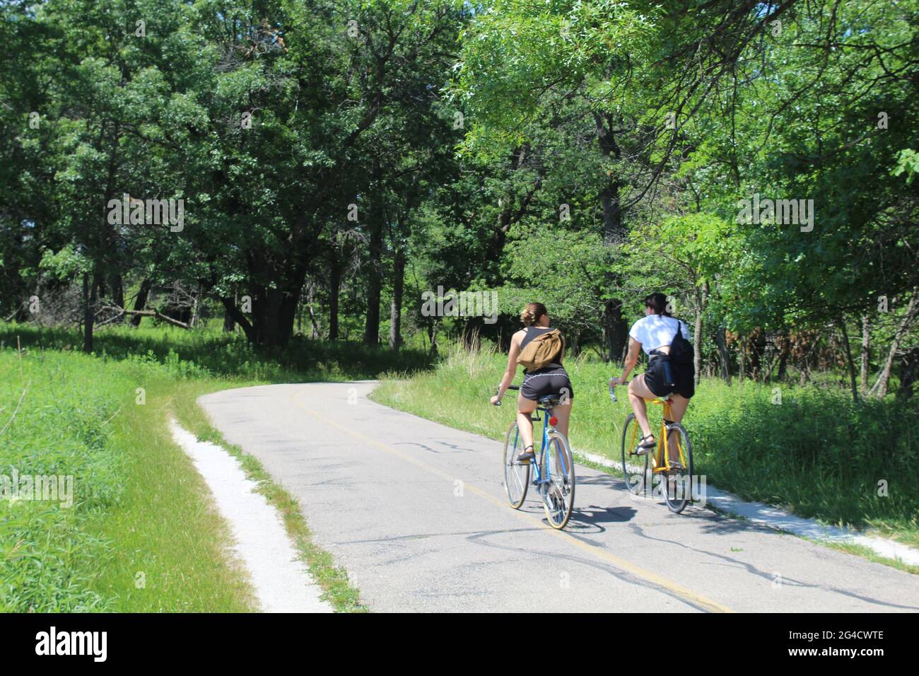 Two young women with backpacks riding bicycles on the North Branch Trail at Miami Woods in Morton Grove, Illinois Stock Photo