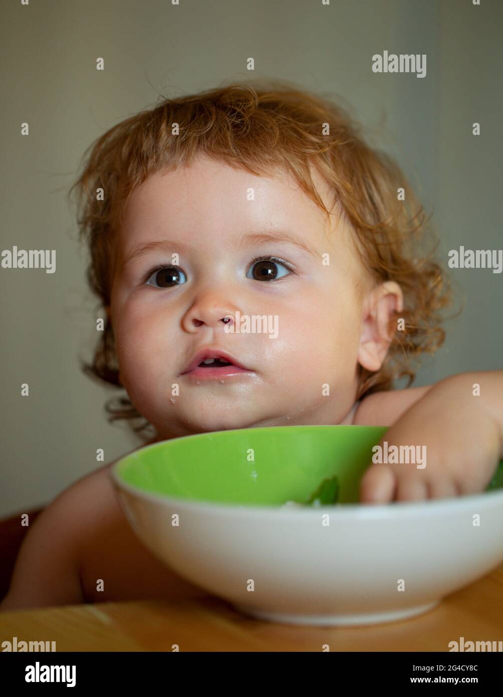 Happy baby eating himself with a spoon. Healthy nutrition for kids. Funny child face closeup. Stock Photo