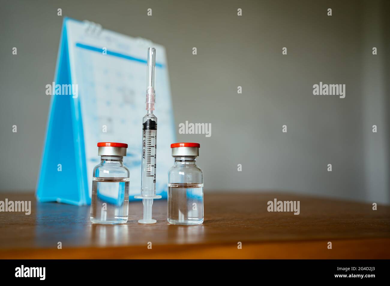 2 vials of vaccine, syringe and a calendar in the background Stock Photo