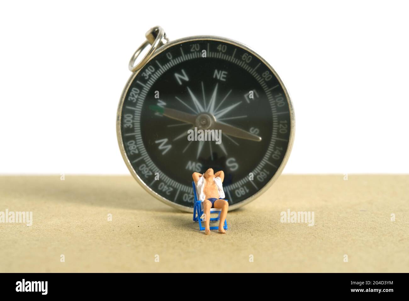 Miniature people toy figure photography. Travel destination, Men relaxing at beach chair with black compass, isolated on white background. Image photo Stock Photo