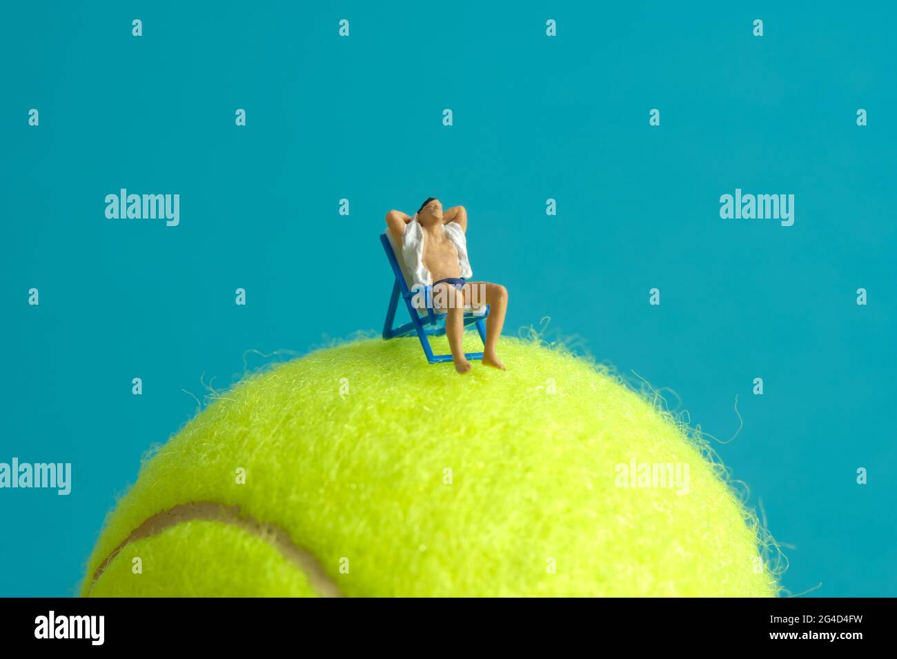 Miniature people toy figure photography. Travel destination concept, Men relaxing at beach chair above tennis ball, isolated on blue background. Image Stock Photo