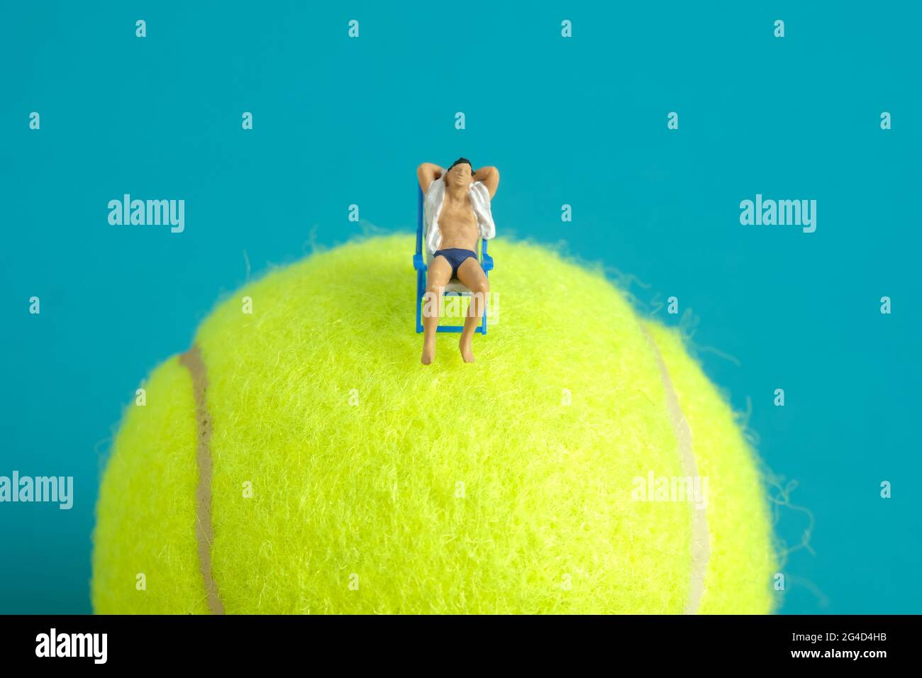 Miniature people toy figure photography. Travel destination concept, Men relaxing at beach chair above tennis ball, isolated on blue background. Image Stock Photo