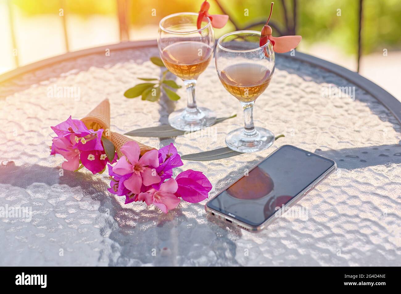 Glasses with homemade liqueur, decorative with fresh summer surreal flowers and mobile phone. Feminine flat lay. Summer bright background for advertis Stock Photo