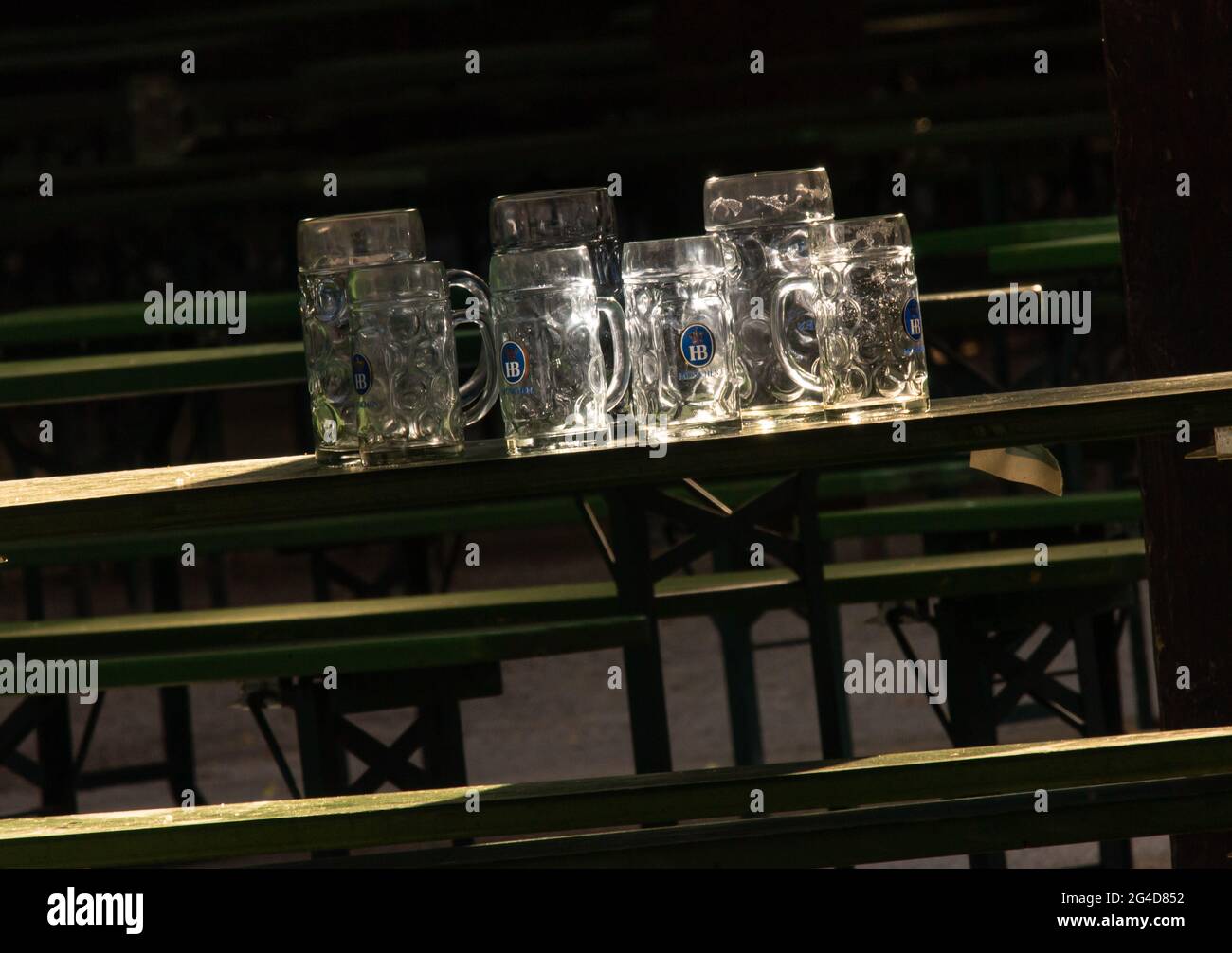 Munich, Germany. 21st June, 2021. Several beer mugs with the Hofbräu München logo stand on a table in the Biergaren at the Chinese Tower in the English Garden in the sun that shines through the glasses. Credit: Peter Kneffel/dpa/Alamy Live News Stock Photo