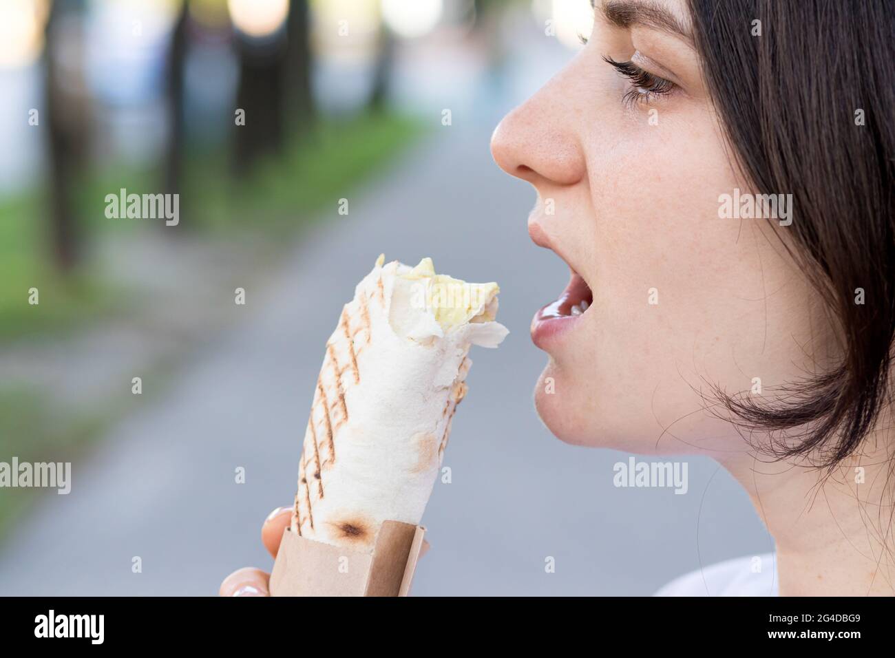Beautiful woman eating shawarma on a city street. Fast food on the way to work or school. Place for text. Stock Photo