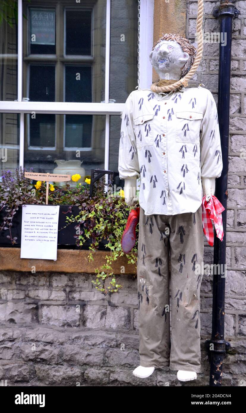 A dummy man hangs with a noose round the neck in Tideswell, Derbyshire, England, United Kingdom as part of the town's Wakes Week, June 19th to 26th, 2021. The notice invites passers-by to guess the name of the man in history it refers to. It refers to Anthony Lingard of Litton who was convicted in 1815 at Derby Assizes of the murder of Hannah Oliver, tollhouse keeper at Wardlow Mires. He was hanged at Derby Jail, and by order of the judge, Sir John Bailey, his body was gibbeted (hung on public display) at Peter’s Stone in Cressbrookdale. Stock Photo