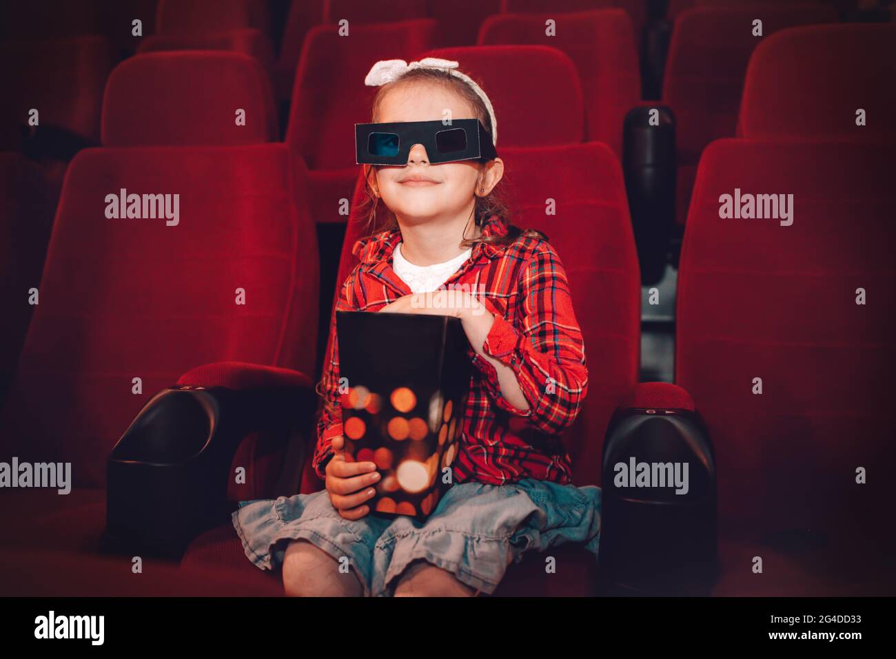 Little girl watching cartoon 3D movie in cinema and eating popcorn Stock Photo