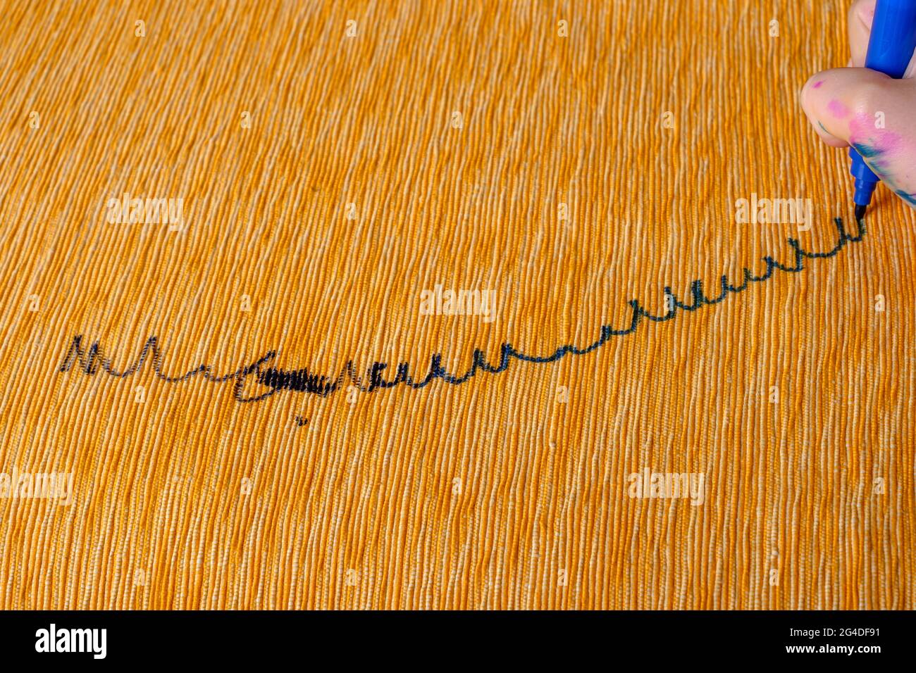 Children's hand draws a felttip pen on the upholstery of the yellow sofa. top view Stock Photo