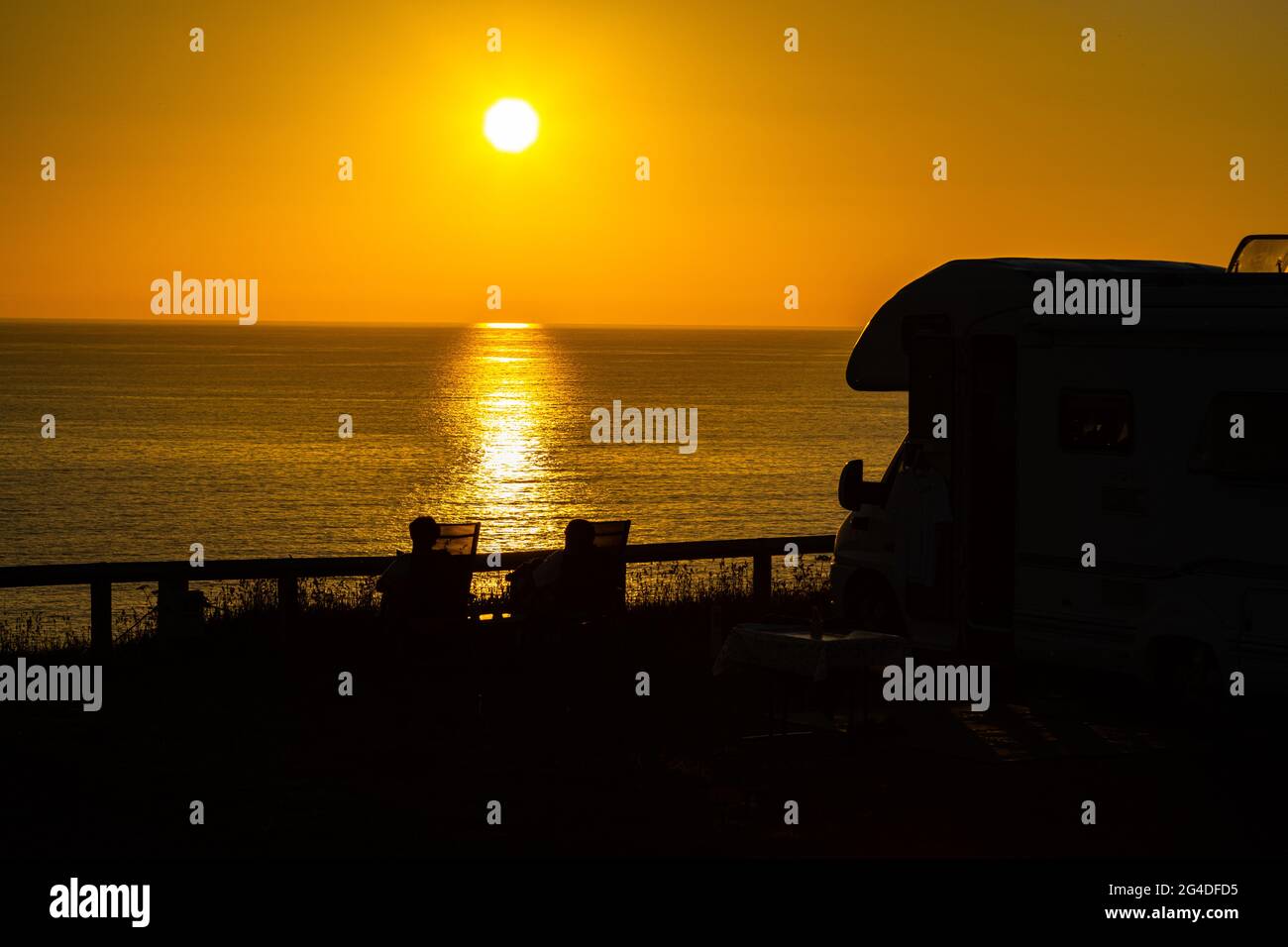 Beautiful golden hour sunset with a couple relaxing next to a camper van and enjoying the summer sunset in Cornwall England UK Stock Photo