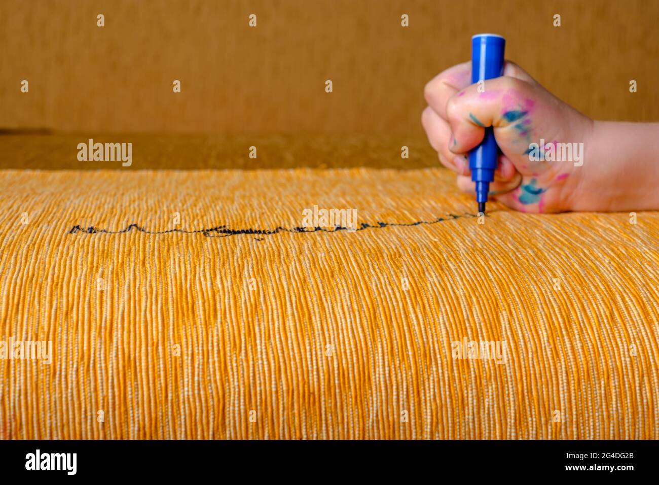 Children's hand draws a felttip pen on the upholstery of the yellow sofa. top view Stock Photo