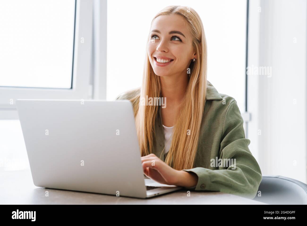 Happy attractive young blonde woman sitting at the table with laptop computer indoors Stock Photo