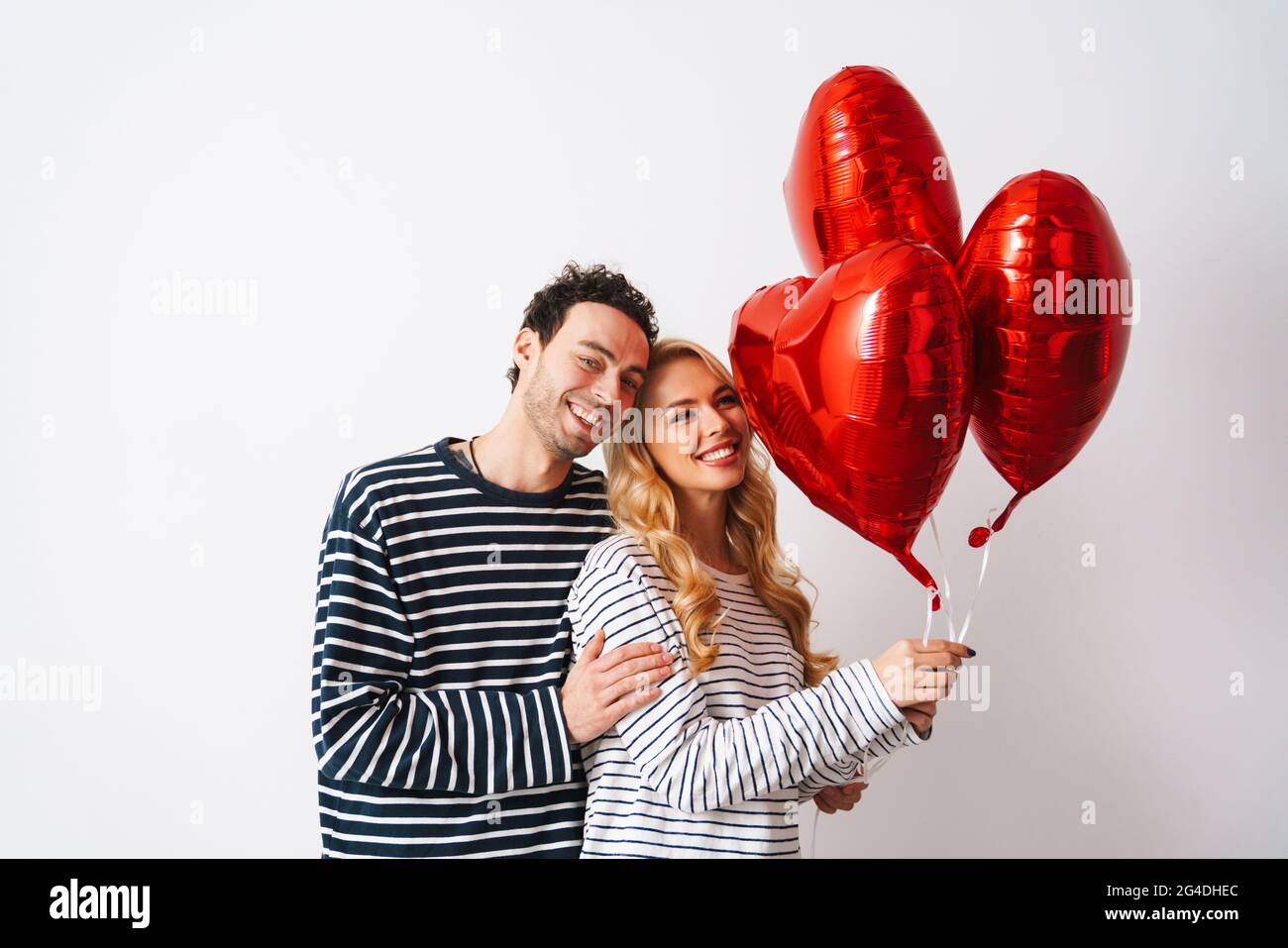 Happy romantic couple smiling while posing with heart balloons isolated ...