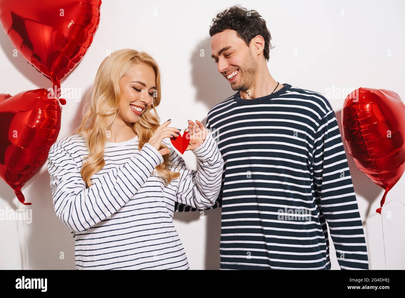 Joyful couple holding valentine card while posing with heart balloons ...