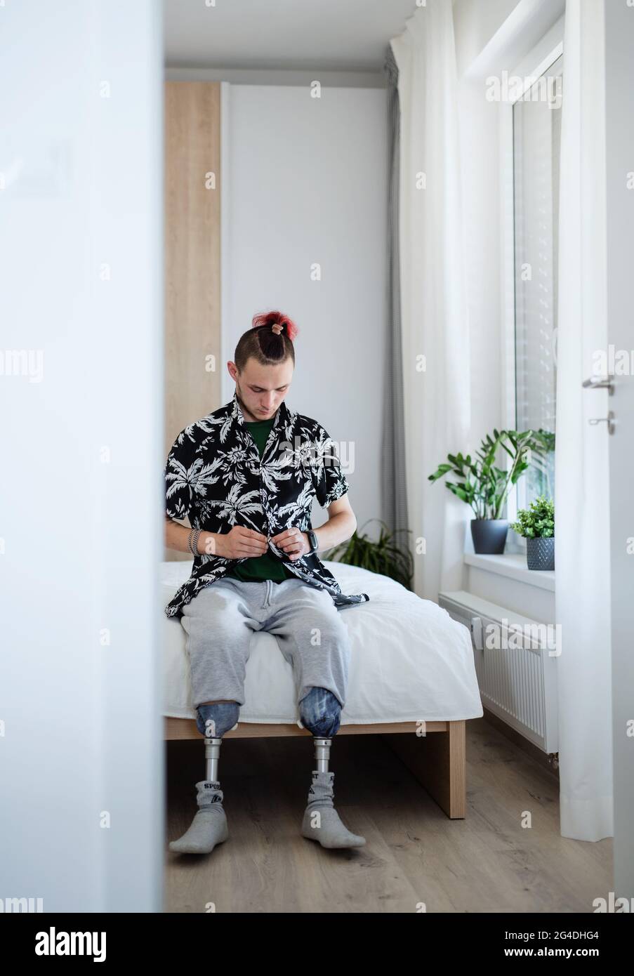 Portrait of disabled young man sitting in bed indoors at home, leg prosthetic concept. Stock Photo