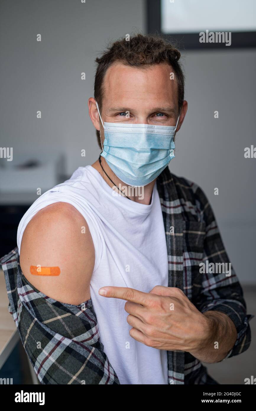 Happy mid adult man after covid-9 vaccination, pointing to plaster on arm and looking at camera. Stock Photo