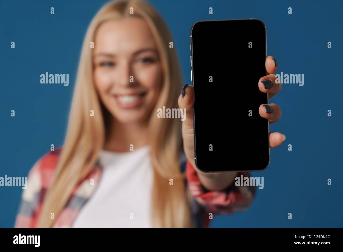 Blonde happy white woman smiling while showing mobile phone isolated over blue background Stock Photo