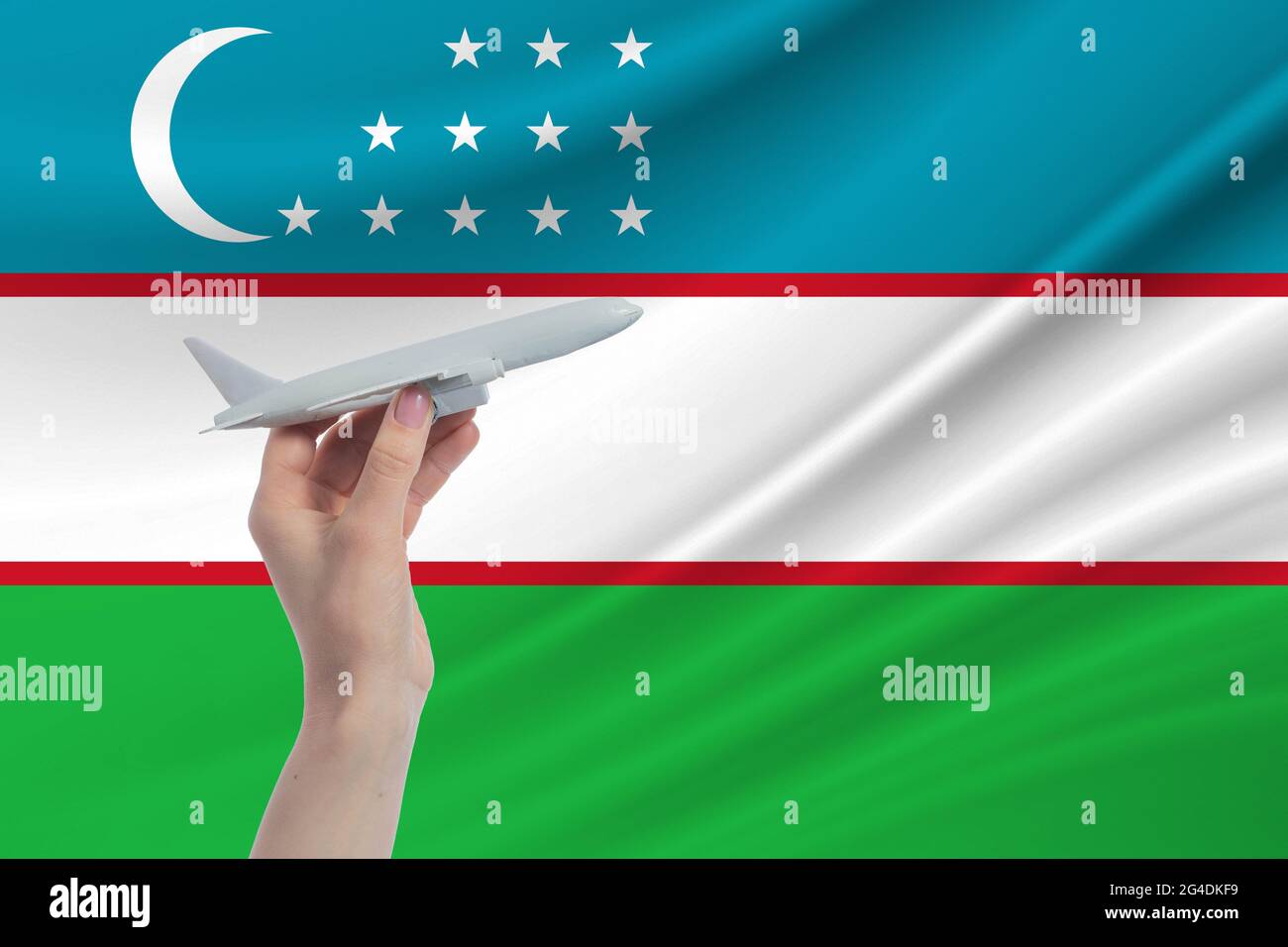 Airplane in hand with national flag of Uzbekistan. Travel to Uzbekistan. Stock Photo