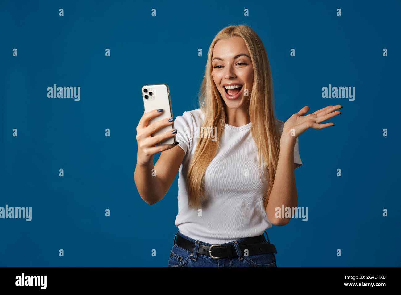 Excited woman holding copyspace while taking selfie on cellphone isolated over blue background Stock Photo