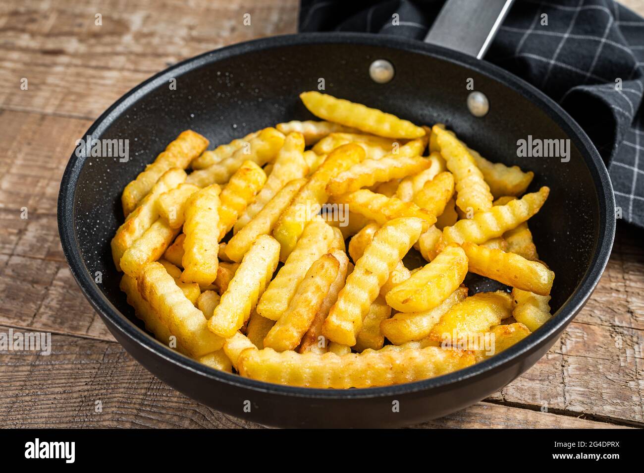 Deep fried Crinkle French fries potatoes sticks in a pan. Wooden