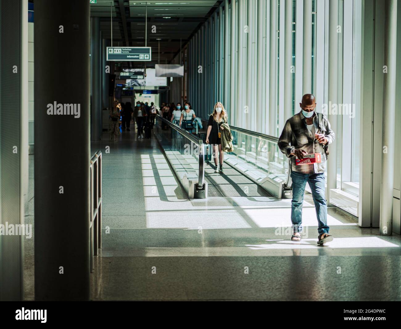 Passengers on travel way at an airport. The passengers all wearing