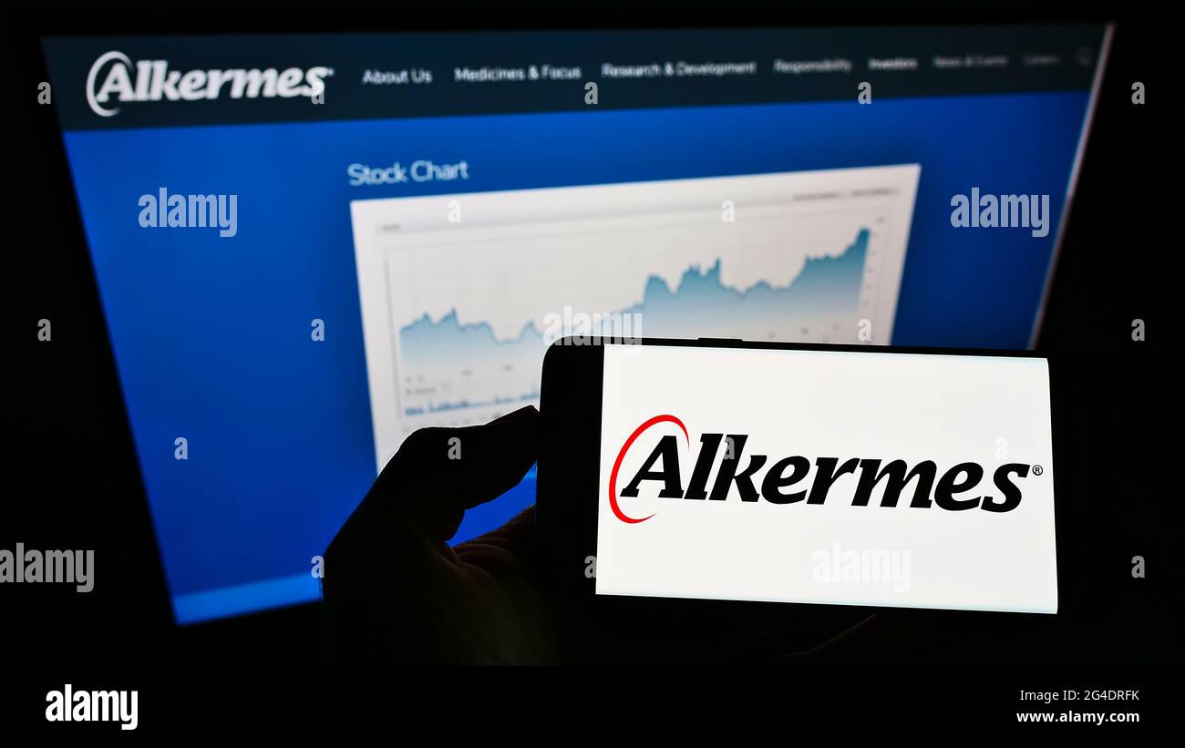 Person holding smartphone with logo of Irish biopharmaceutical company Alkermes plc on screen in front of website. Focus on phone display. Stock Photo