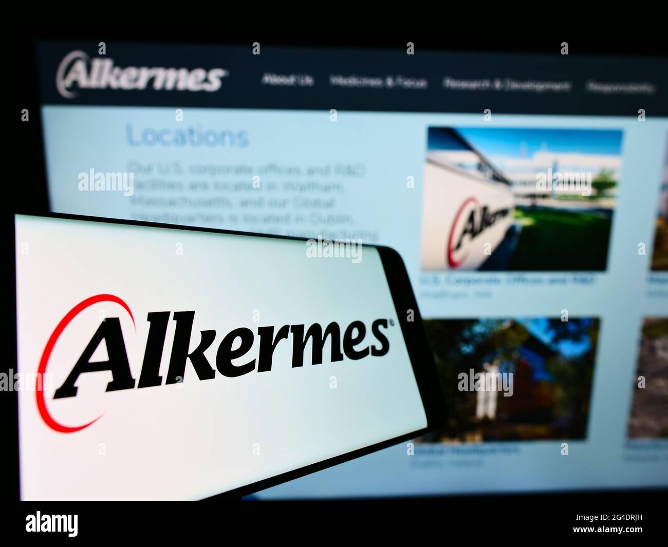 Mobile phone with logo of Irish biopharmaceutical company Alkermes plc on screen in front of website. Focus on center-right of phone display. Stock Photo