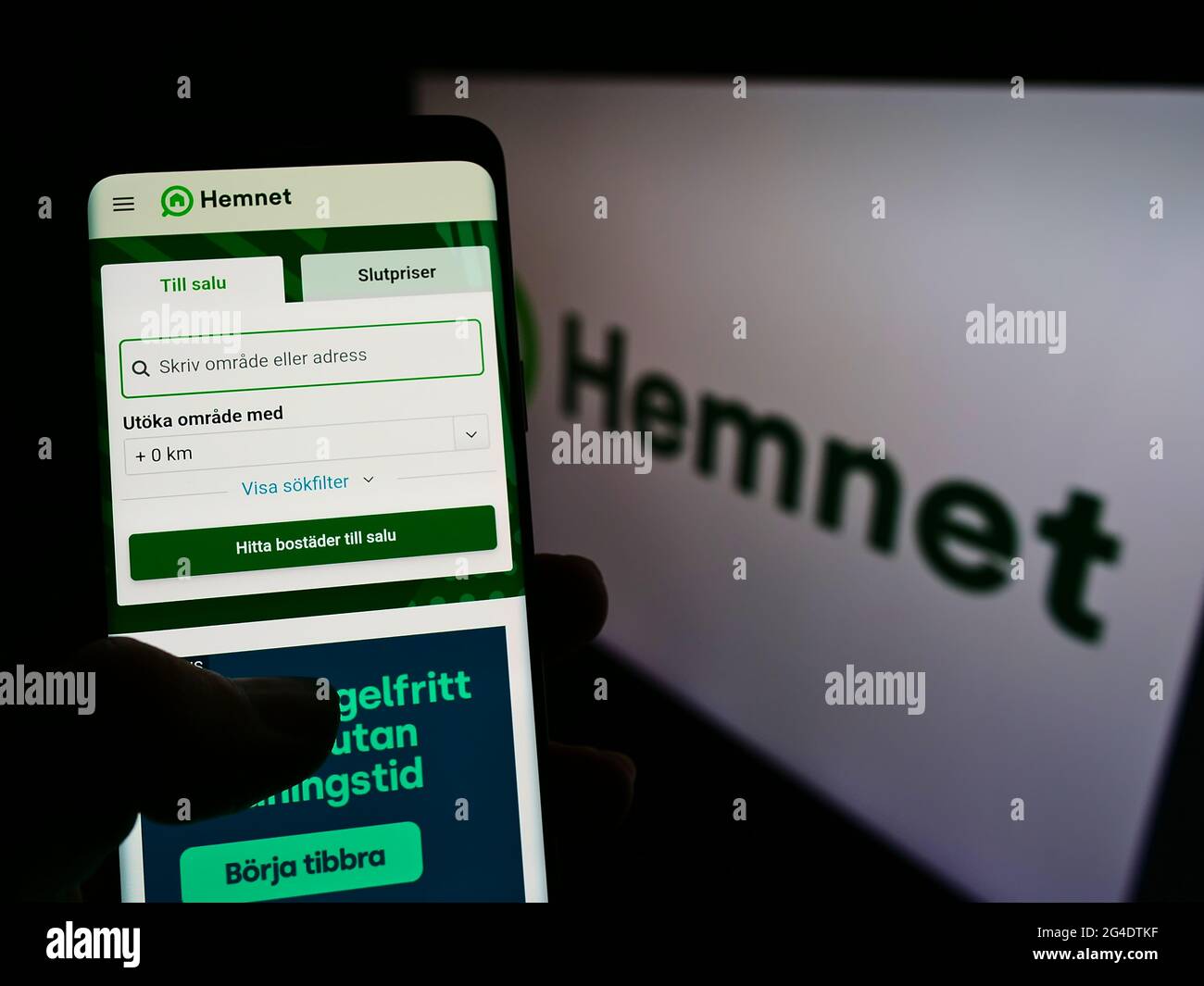 Person holding smartphone with website of Swedish property platform company Hemnet AB on screen in front of logo. Focus on center of phone display. Stock Photo